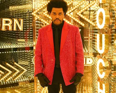 Musician in a red jacket stands in a mirrored, illuminated room resembling a funhouse at a performance event.