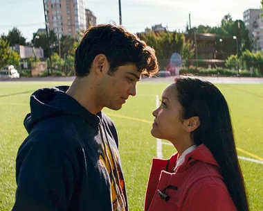 A young couple stands facing each other on a soccer field, sharing an intimate moment under the sun.