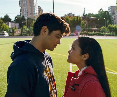 A young couple stands facing each other on a soccer field, sharing an intimate moment under the sun.