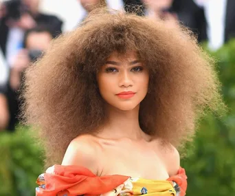 A woman with voluminous curly hair and an off-the-shoulder floral dress at a formal event.