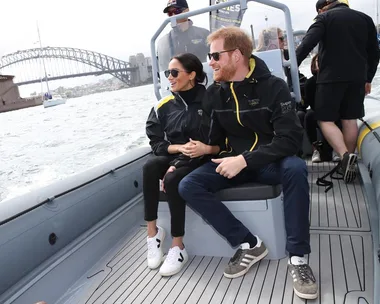 A couple sits on a boat near a bridge, both wearing casual sportswear and sunglasses.