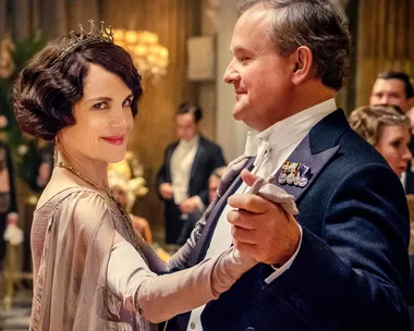 A couple in elegant attire dances in a lavish ballroom setting.