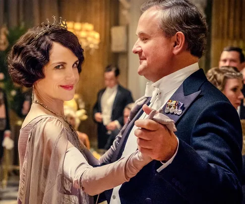 A couple in elegant attire dances in a lavish ballroom setting.