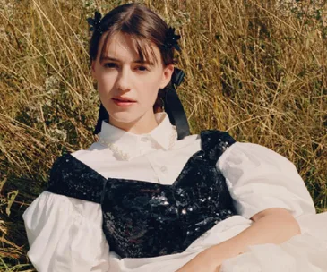 Model in Simone Rocha x H&M outfit with black sequined top over white blouse, lying in grass.