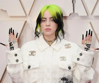 Person with black and neon green hair wearing a white jacket, showcasing intricate rings and long black nails.