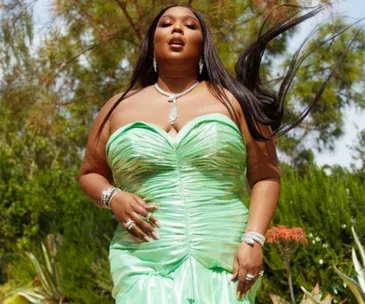 Singer wearing a green strapless dress and silver jewelry, posing outdoors with trees in the background at the 2021 Grammys.