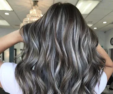 Gray-blended hair trend with long, wavy strands in a salon setting, showcasing silver and dark tones.