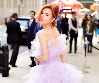 Woman in a flowing lavender gown poses on a bustling city street, with a playful expression.