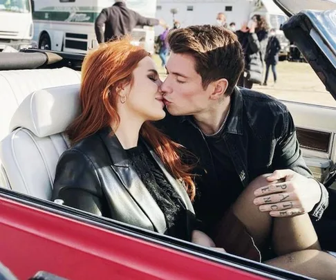 A couple kisses in a convertible car, with the man showing tattoos on his hand.