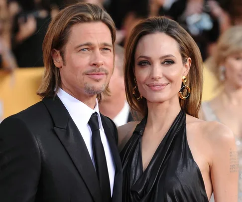 A man in a black suit and a woman in a black dress smile at an event, posing side by side, with a blurred crowd in the background.