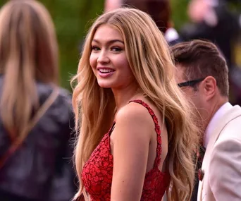 A woman with long blonde hair smiles in a red lace dress at an outdoor event.