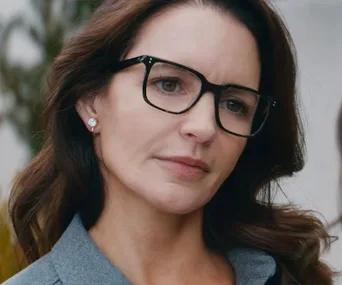 A woman with dark hair and glasses looks thoughtful, possibly a scene from "Deadly Illusions."