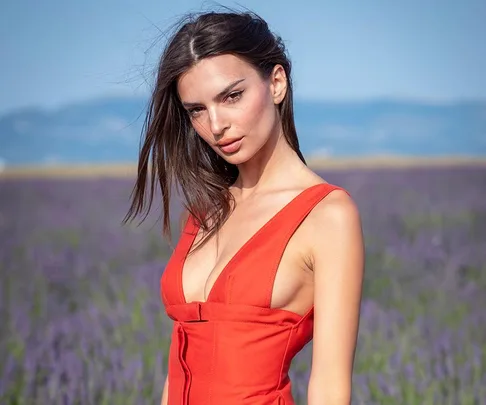 Woman in a red dress standing outdoors with a lavender field and mountains in the background.