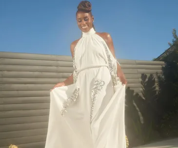 Smiling woman in a white halter dress with silver embellishments, standing outside in daylight.