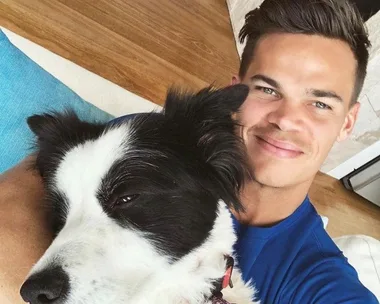 A man smiling while lying on the floor, cuddling a black and white dog.