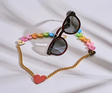 Sunglasses with a rainbow heart chain, featuring gold accents and reflective lenses, on a white background.