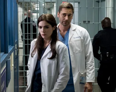 Doctors in white coats stand in a corridor, with jail cells in the background.