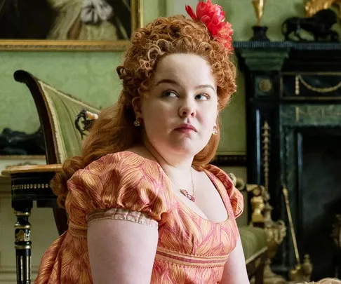 Nicola Coughlan as Penelope Featherington in a Regency-era dress from "Bridgerton," sitting in an ornate room.