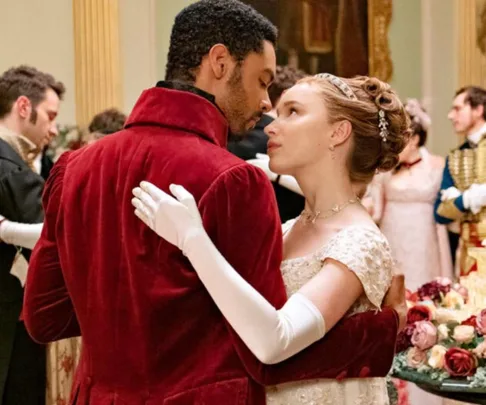 A couple in period attire dance intimately at a ballroom event, surrounded by elegantly dressed guests.