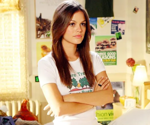 Summer Roberts from "The OC" stands with arms crossed, wearing a white T-shirt in a poster-decorated room.