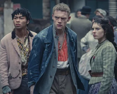 Three characters from "The Irregulars" stand in Victorian attire, looking alert in a crowded street.