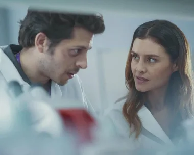 Two scientists wearing lab coats share a serious conversation in a laboratory setting.