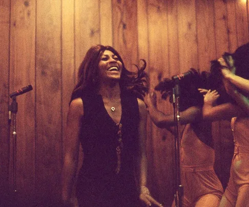 Tina Turner performs energetically, smiling with backup dancers onstage.