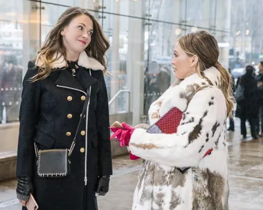 Two women in winter coats having a conversation in an urban setting.