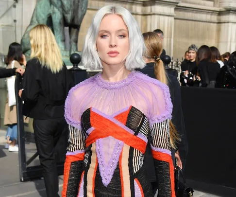 A woman with short, silver hair in a colorful, patterned dress at an outdoor event surrounded by people.