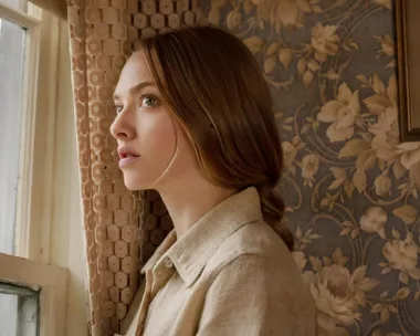 A woman gazes out a window in a floral wallpapered room, from the movie "Things Heard & Seen."