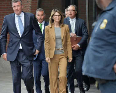 A group of people in business attire walk outside a building, surrounded by security.