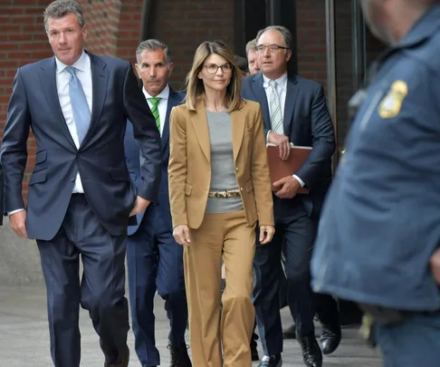 A group of people in business attire walk outside a building, surrounded by security.