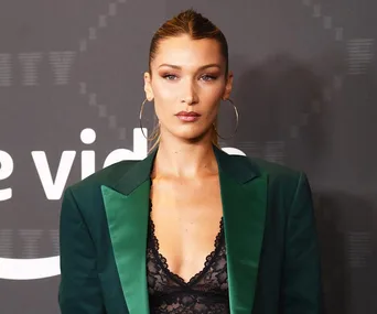 Model wears hoop earrings, a dark green blazer with a lace top, standing in front of a dark backdrop with text.