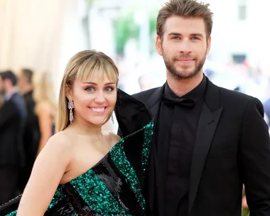 A couple poses at a formal event, with the woman in a green and black dress and the man in a black suit and bow tie.