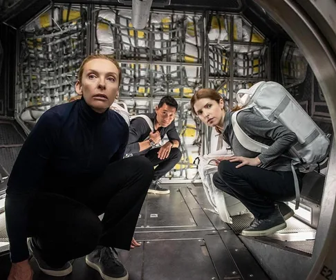 Three astronauts crouch in a spacecraft corridor, looking alert and tense, from the movie "Stowaway."