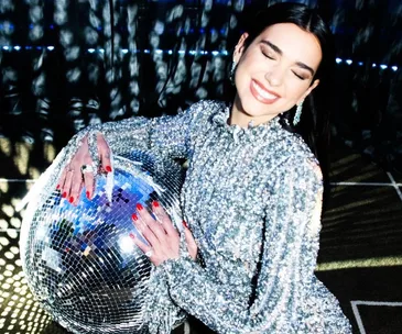 A woman in a shimmering silver outfit smiles while holding a disco ball at an Oscars 2021 after-party.