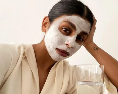 Person with a white face mask, resting head on hand, next to a glass of water.