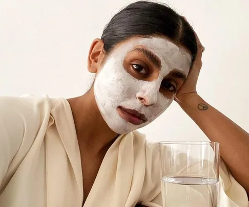 Person with a white face mask, resting head on hand, next to a glass of water.