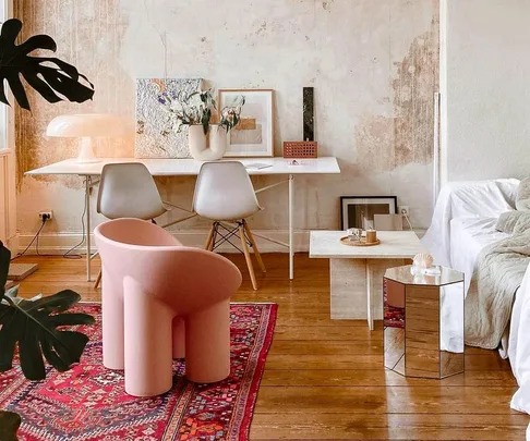 Cozy living room with a pink roly-poly chair, wooden floor, red rug, modern decor, and white desk with art.