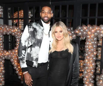 A man and woman pose together at an event with decorative balloons in the background.