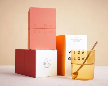 "Stacked Vida Glow Marine Collagen boxes beside a glass with spoon on table."