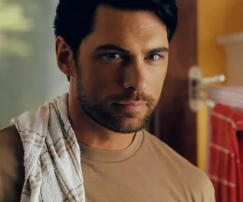 A man with a towel over his shoulder stands in a room with red kitchen towels, looking intently ahead.