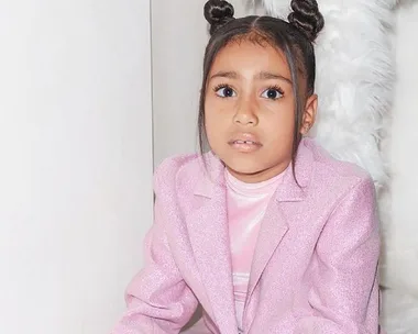 Young girl with space buns in a sparkly pink outfit, sitting against a white background.