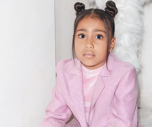 Young girl with space buns in a sparkly pink outfit, sitting against a white background.