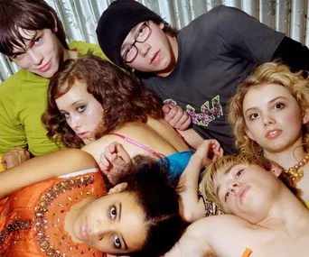 A group of young people from the TV show "Skins" lie together on a bed, looking at the camera.