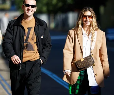 Two stylish individuals at Australian Fashion Week 2021; one in sunglasses and a sweater, the other in a blazer and sunglasses.