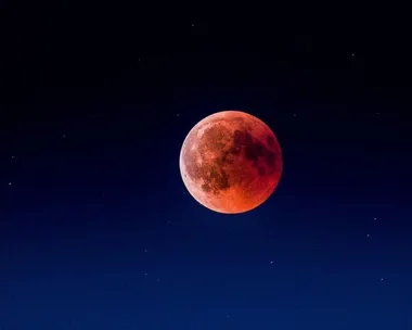 Super Blood Moon glowing red in a dark night sky with scattered stars.