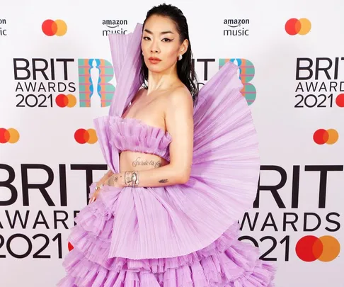 Person in a purple pleated dress poses on the BRIT Awards 2021 red carpet.