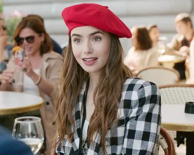 Emily in a red beret and checkered jacket sits at an outdoor cafe in "Emily in Paris" Season 2.