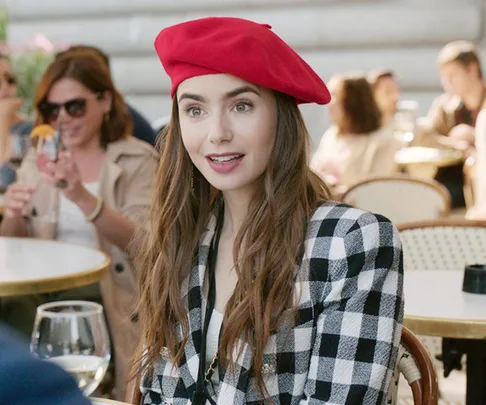 Emily in a red beret and checkered jacket sits at an outdoor cafe in "Emily in Paris" Season 2.